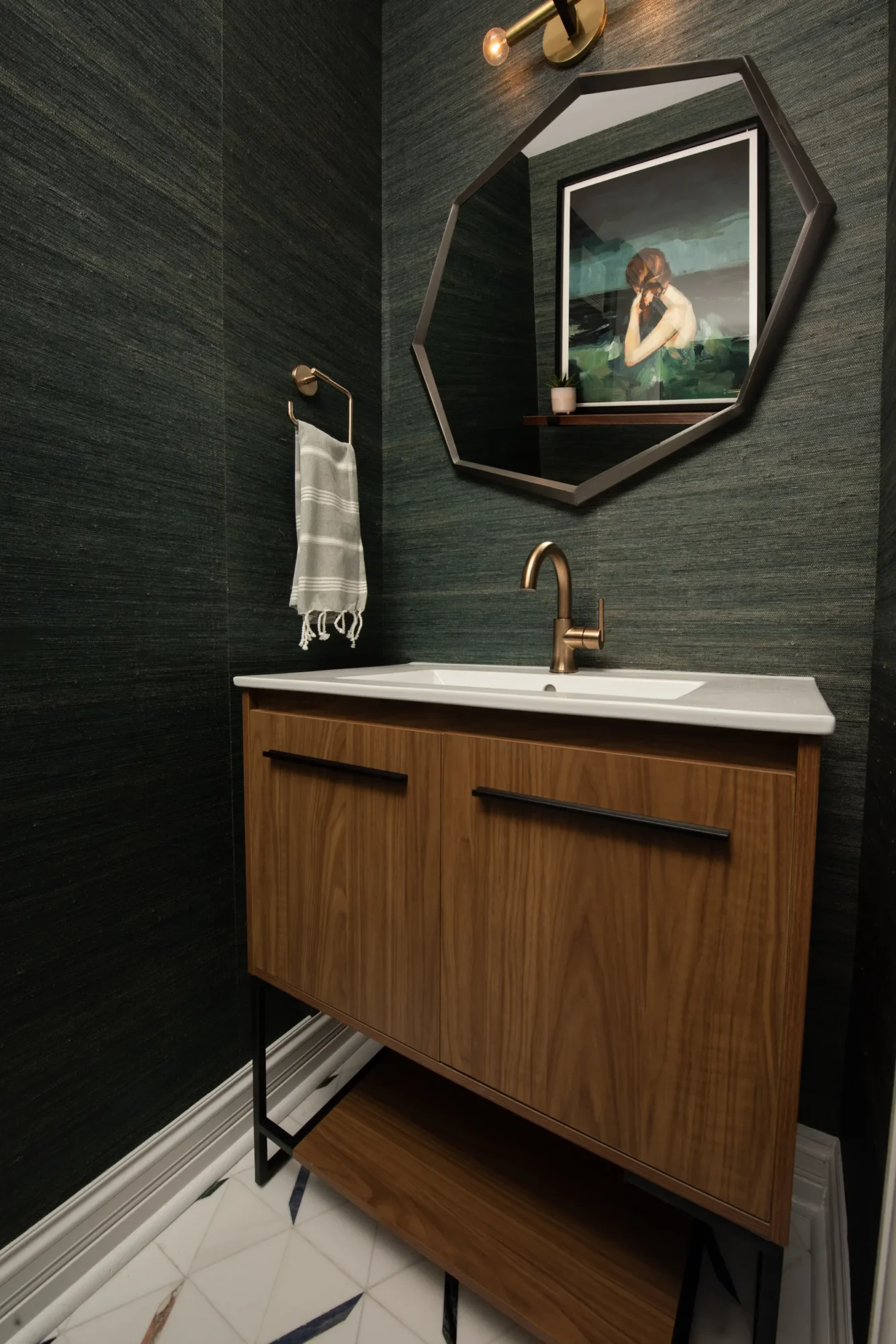 Mid-century modern powder room with octagonal mirror, teak vanity, brass fixtures, textured dark walls, and geometric tile flooring.