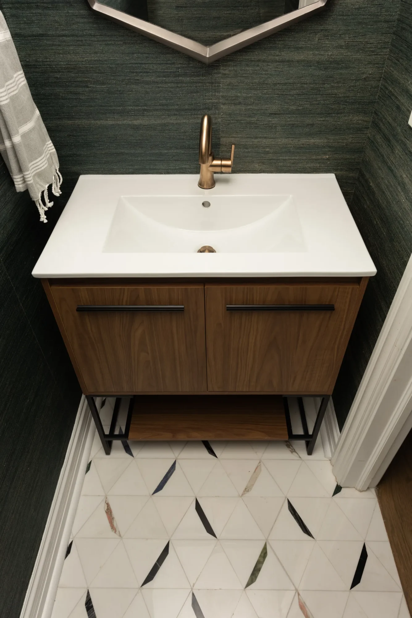 Mid-century modern powder room with geometric mirror, walnut vanity, brass faucet, textured walls, and patterned tile flooring.