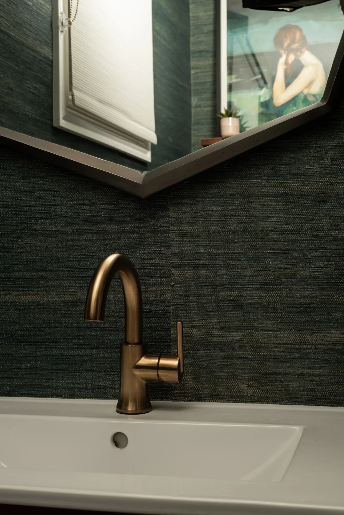 Contemporary powder room with geometric mirror, textured dark walls, sleek bronze faucet, and minimalist sink.