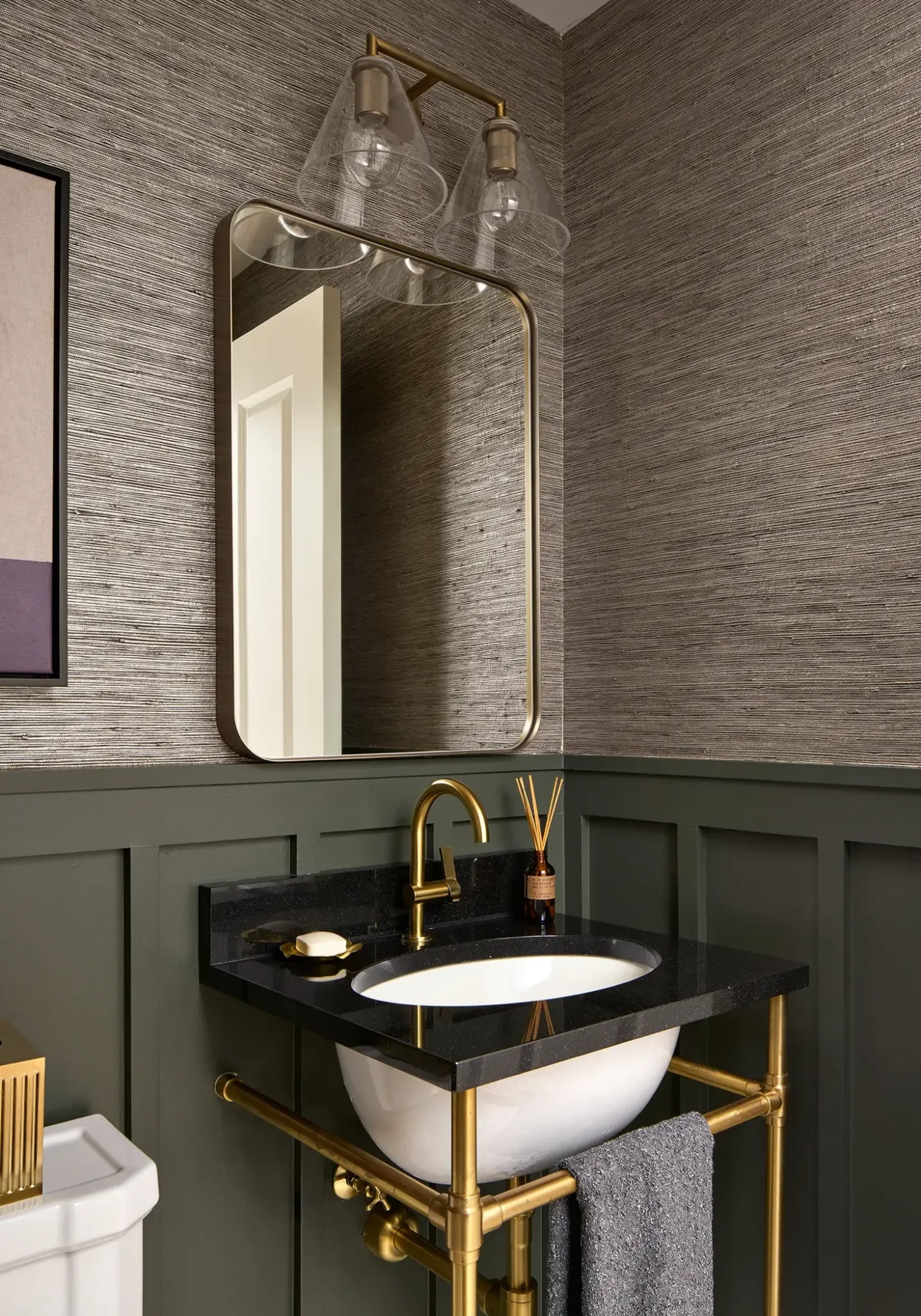 High-end Chicago powder bath with brass console sink, black stone top, olive wainscoting, and gray-brown grasscloth.