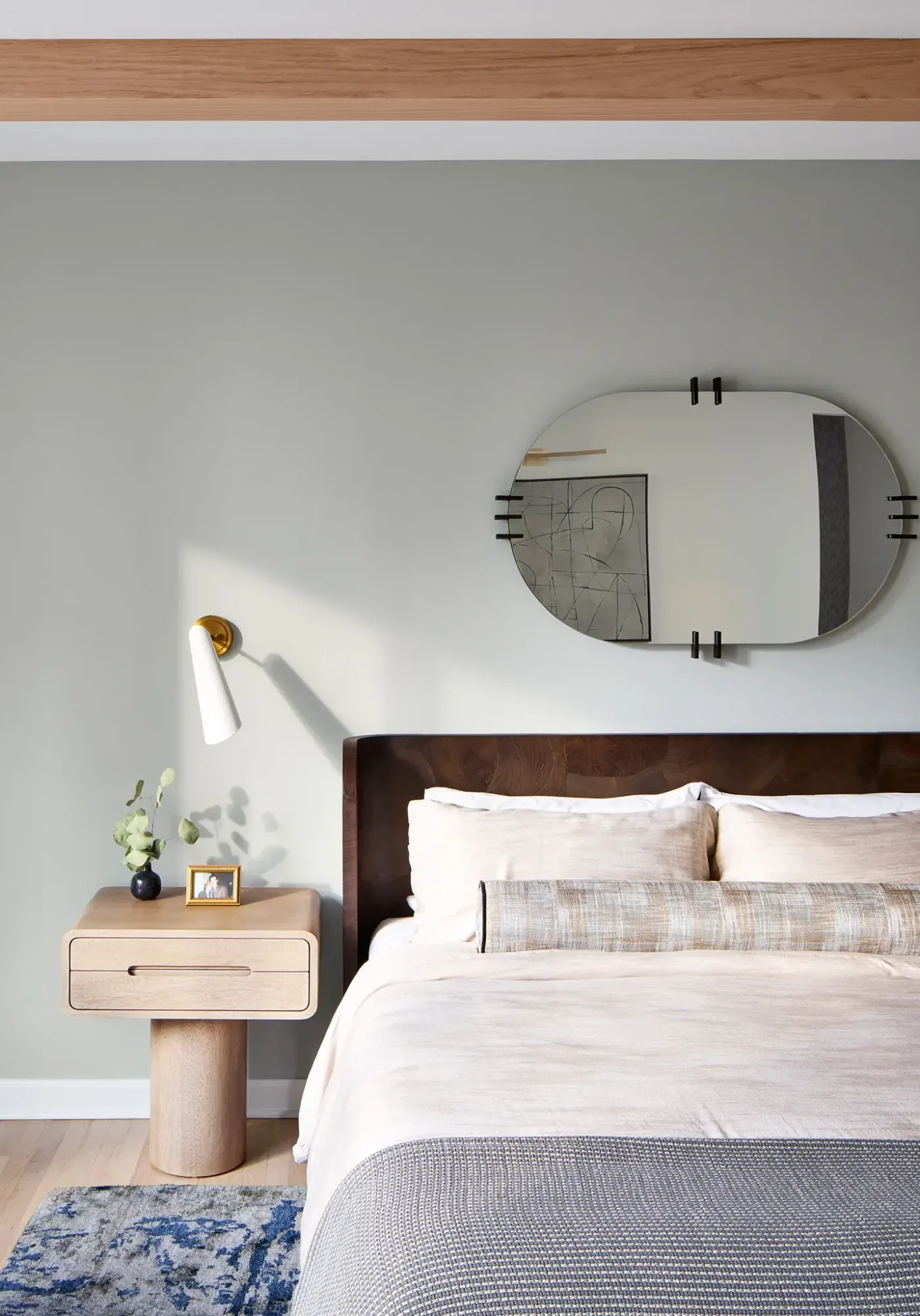Luxury Streeterville Chicago bedroom with sage wall, light-oak nightstand, brass sconce, layered bedding, and oval mirror.