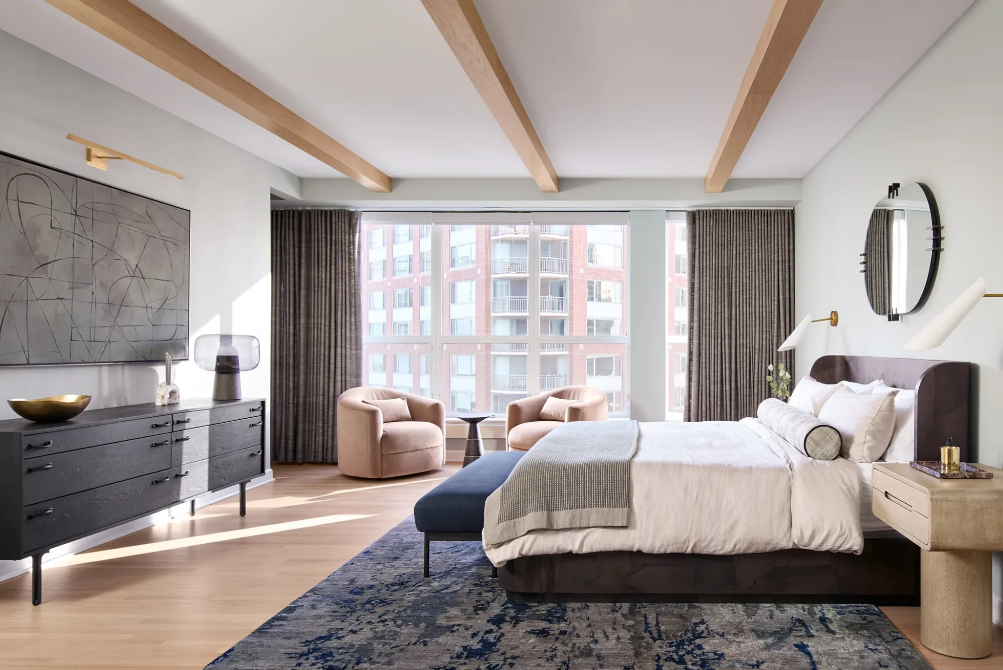 Luxury Streeterville bedroom with window wall, blackout drapery, swivel chairs, upholstered platform bed, light oak floor, and blue abstract rug.