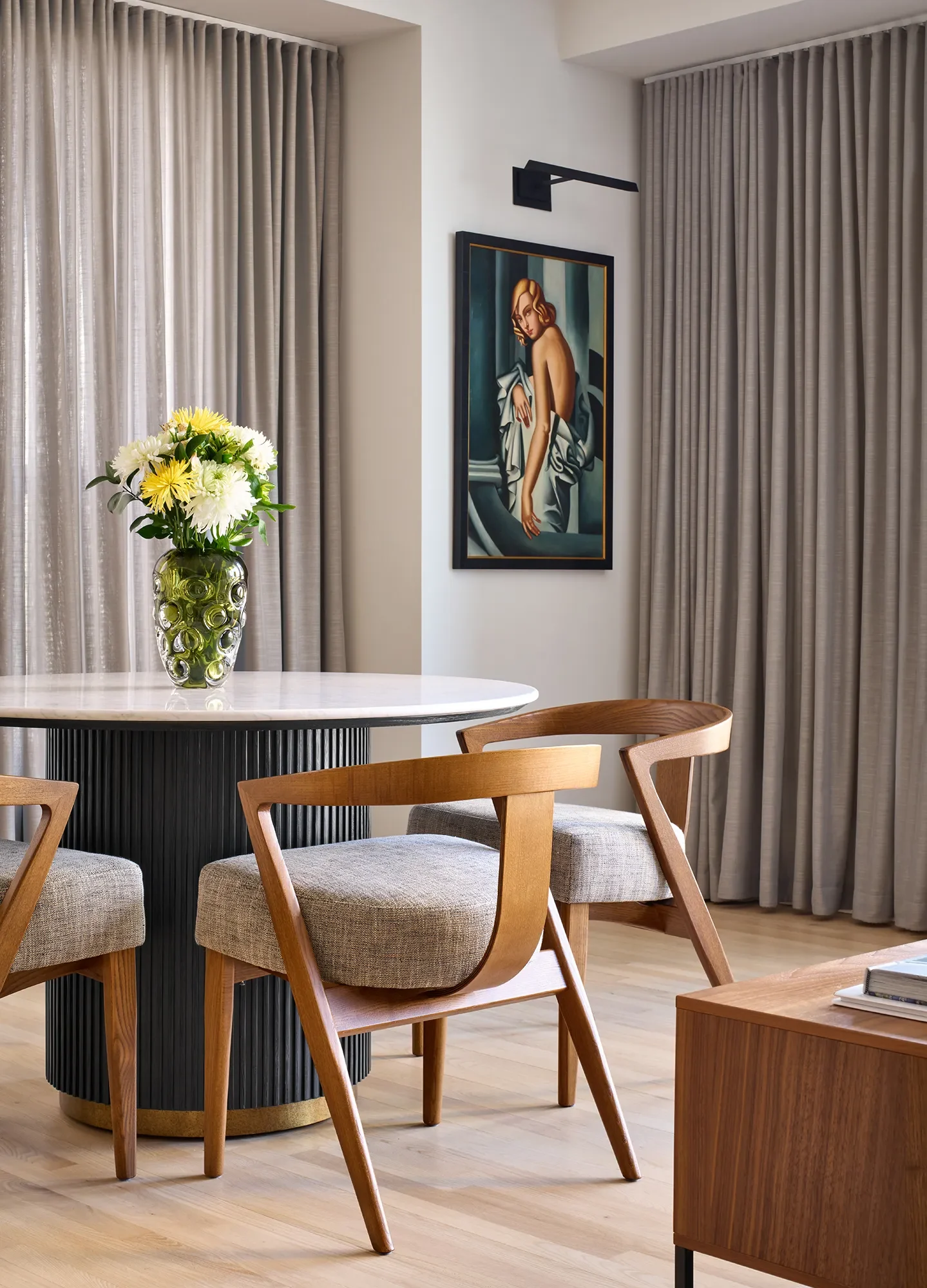 Luxury Streeterville Chicago dining nook with round white pedestal table, mid-century wood chairs, light oak floors, and gray pinch-pleat drapery.