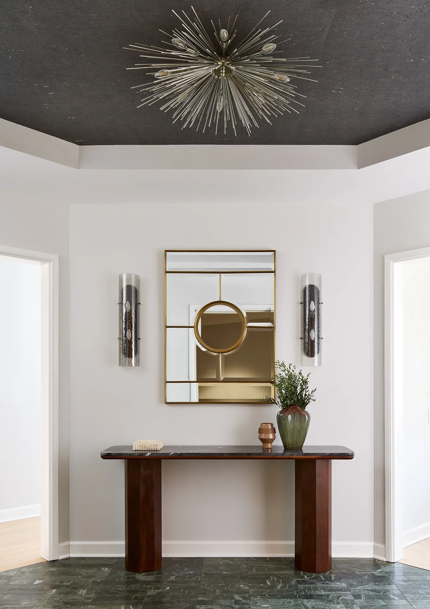Luxury Streeterville Chicago entry alcove with dark Parsons console, brass-grid mirror, smoked-glass sconces, and green stone flooring.