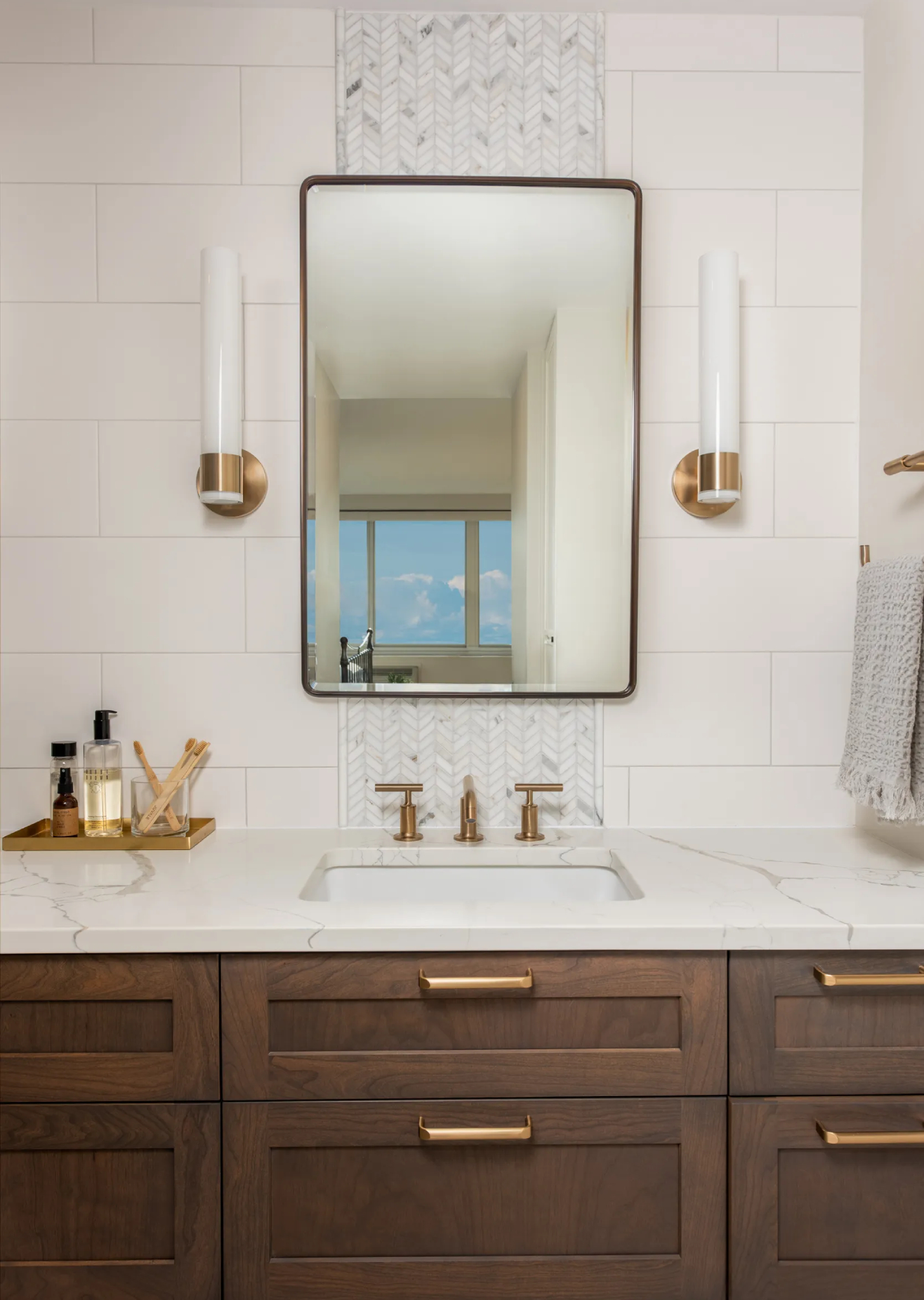 Transitional primary bathroom with elegant vanity, marble countertop, sleek mirror, and brass fixtures. Distinctive chevron tile adds unique character.