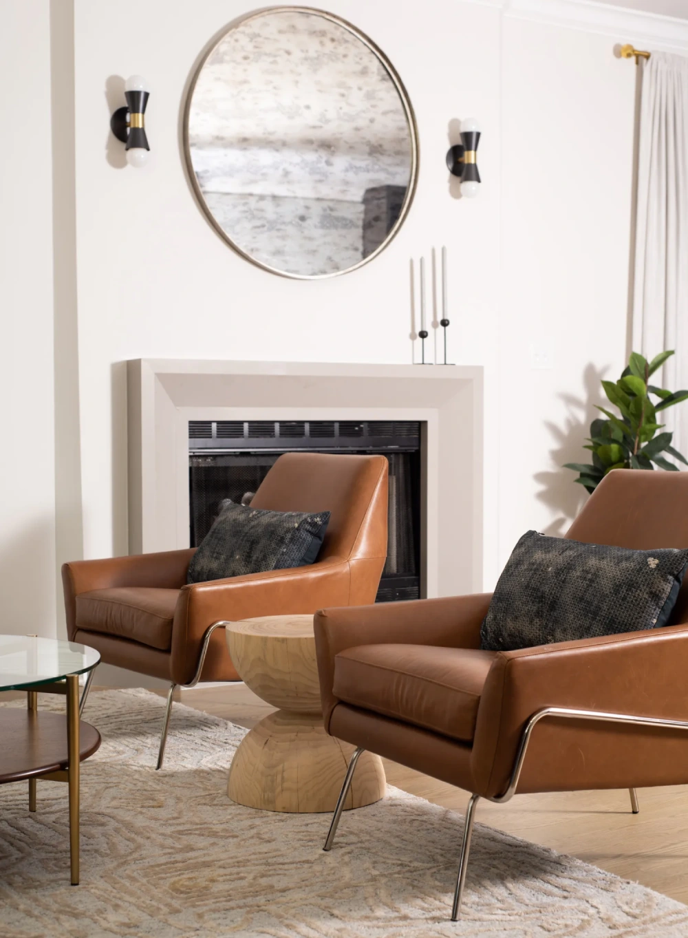 Mid-century modern living room with leather armchairs, sleek fireplace, circular mirror, sculptural side table, and elegant wall sconces.