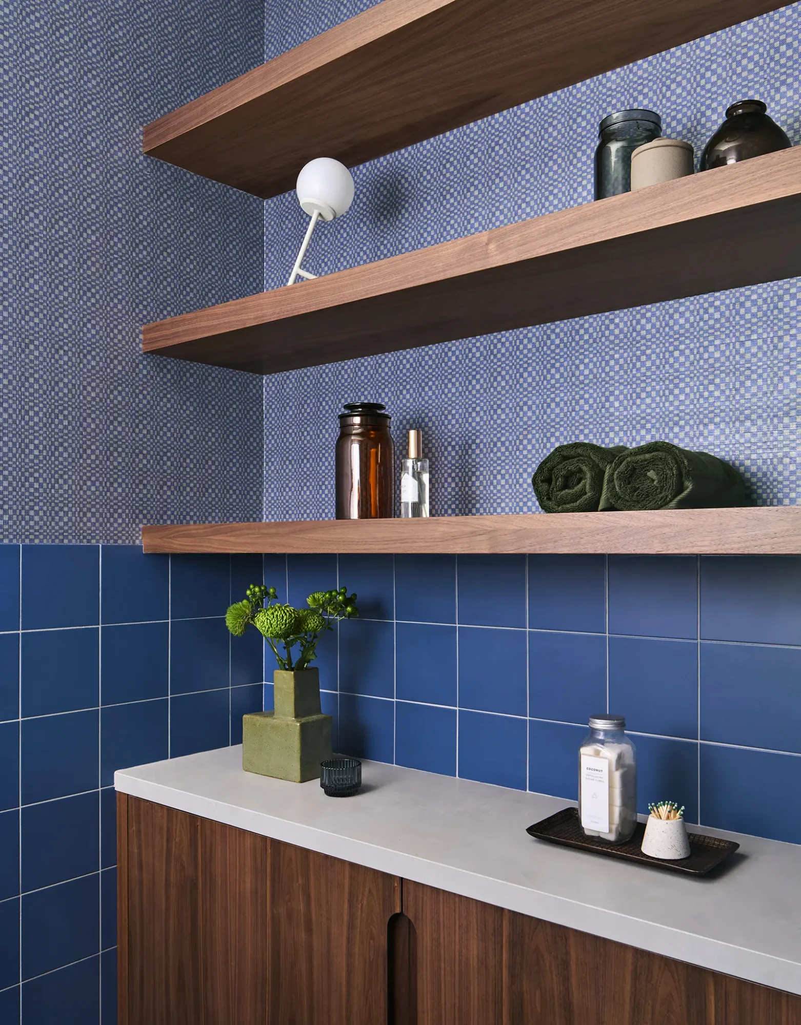 Rich walnut shelving contrasts with a detailed blue mosaic tile wall, creating functional storage and visual interest in a luxury bathroom.